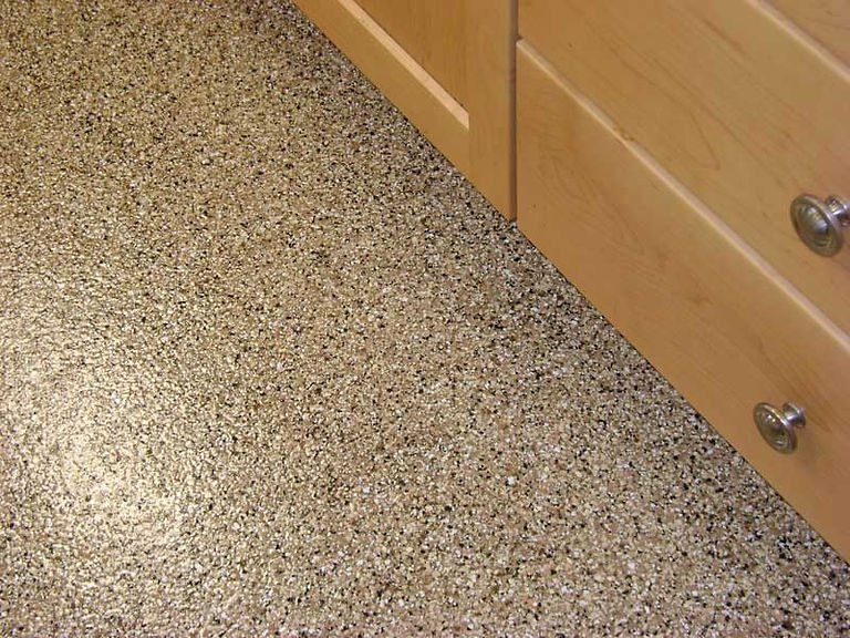 Granulated flooring next to a light-colored wooden cabinet with metal knobs.