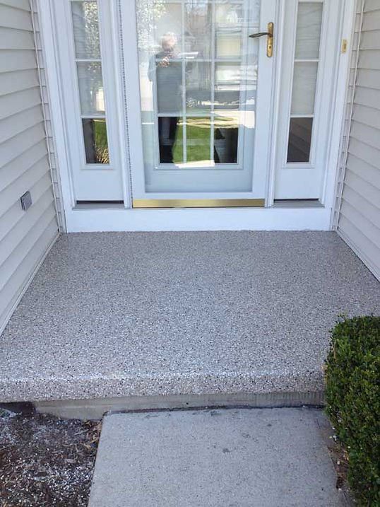 Concrete front porch with textured finish, by a white door with sidelights.
