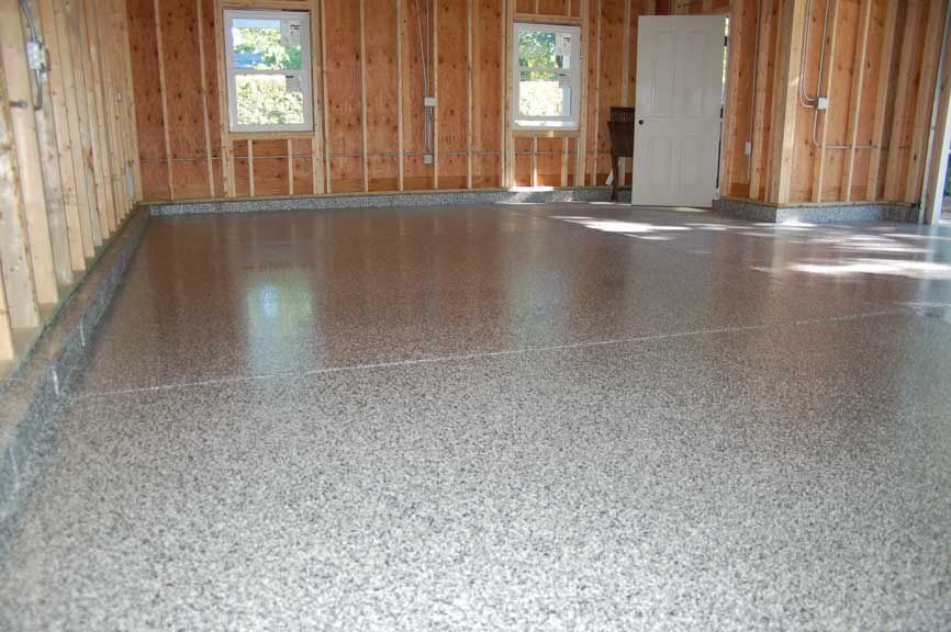 Garage interior with a finished, speckled floor, wooden walls, and windows.