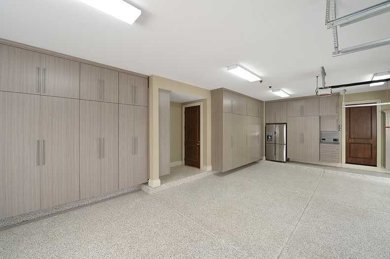 Garage interior with beige storage cabinets, stainless steel refrigerator, and epoxy floor.