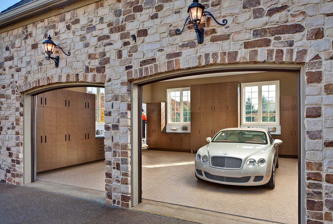 Two-car garage with stone exterior, a silver car inside one bay, and storage cabinets.