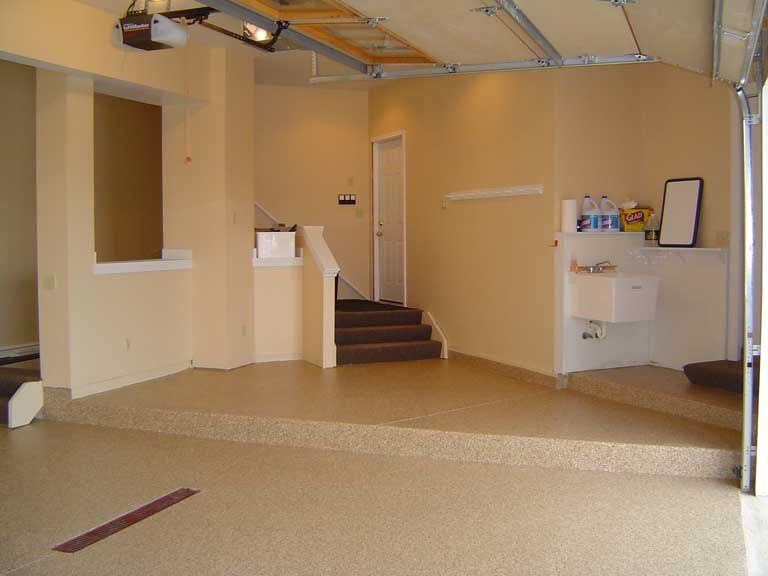 Empty garage interior with beige speckled flooring, stairs, and a utility sink.