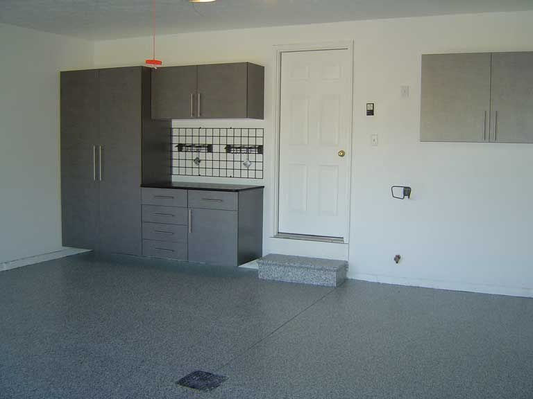 Garage with gray cabinets, white door, and speckled gray floor.