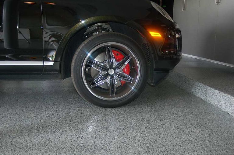 Black SUV with chrome rims and red brake calipers parked on a speckled gray garage floor.