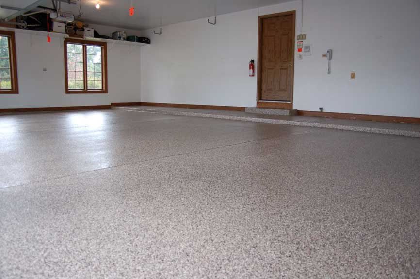 Spacious, empty garage with speckled flooring, white walls, brown trim, windows, and a door.