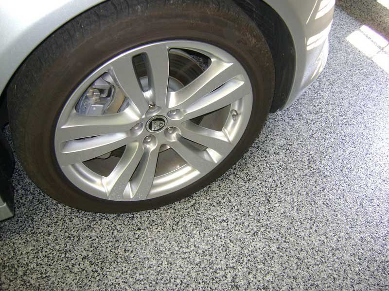 Silver car wheel on a speckled gray garage floor.