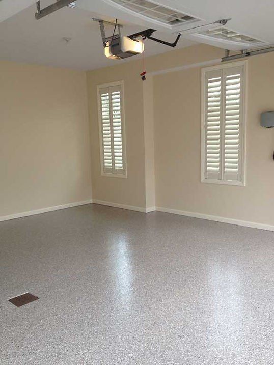 Empty garage with beige walls, two shuttered windows, and a speckled gray floor.