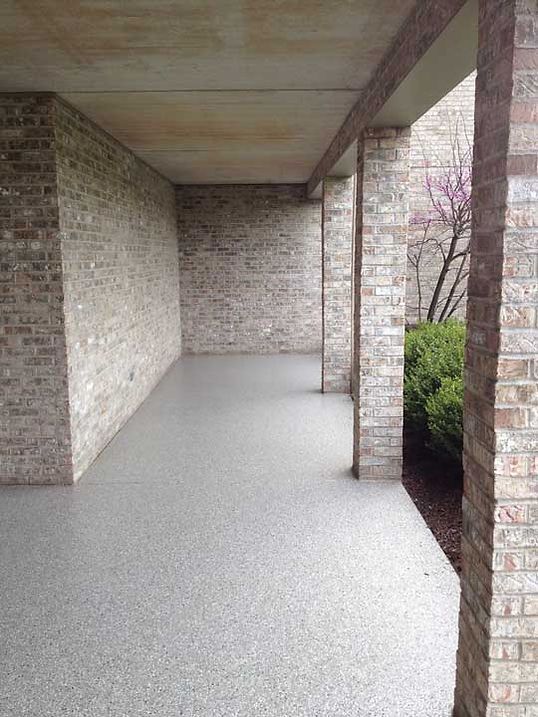 Covered porch with gray speckled flooring, brick walls, and columns.
