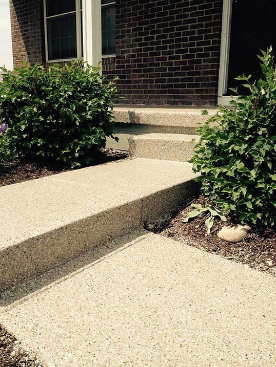 Concrete walkway and steps leading to a brick building entrance, flanked by bushes.