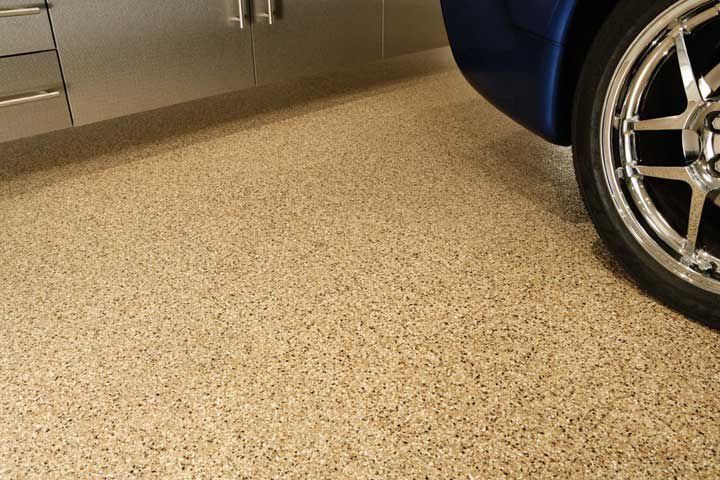 Tan epoxy garage floor with a blue car and cabinets.