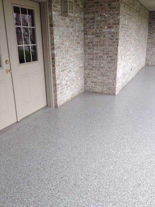 Gray speckled concrete patio with light brick wall and beige door.