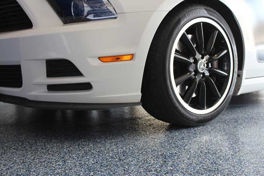 White car's front with black rim tire on speckled blue garage floor.