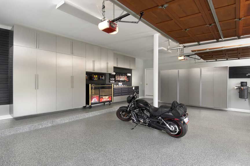 Modern garage with gray epoxy floor, cabinets, motorcycle, and storage.
