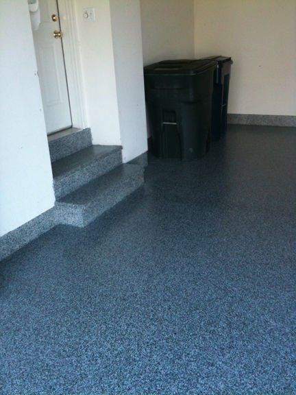 Garage with dark speckled floor, steps, doorway, and black trash bins.
