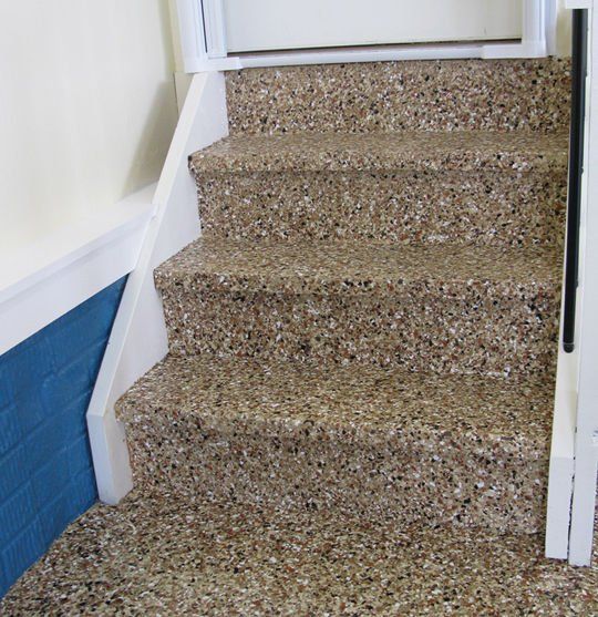 Stairs with speckled flooring leading up to a white door frame. White side panels. Blue wall on the left.
