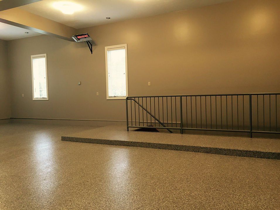 Spacious room with a shiny speckled floor, beige walls, windows, and a metal railing.
