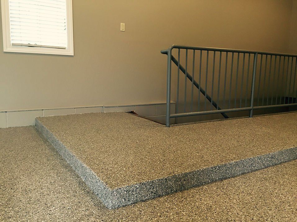 Tan speckled floor with a step up to a platform with a metal railing. Window and neutral walls.