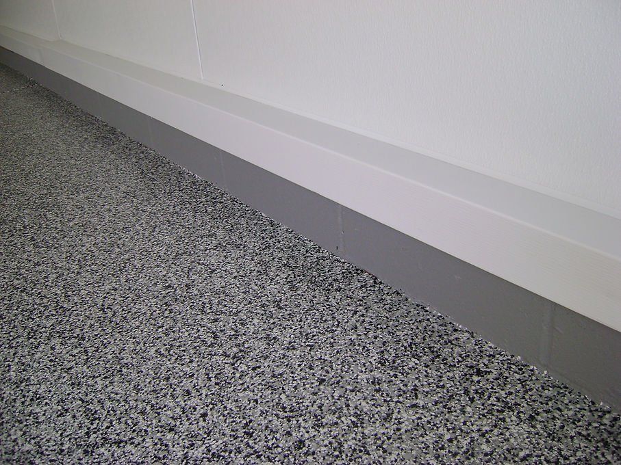 Gray speckled flooring with a gray baseboard and white wall.
