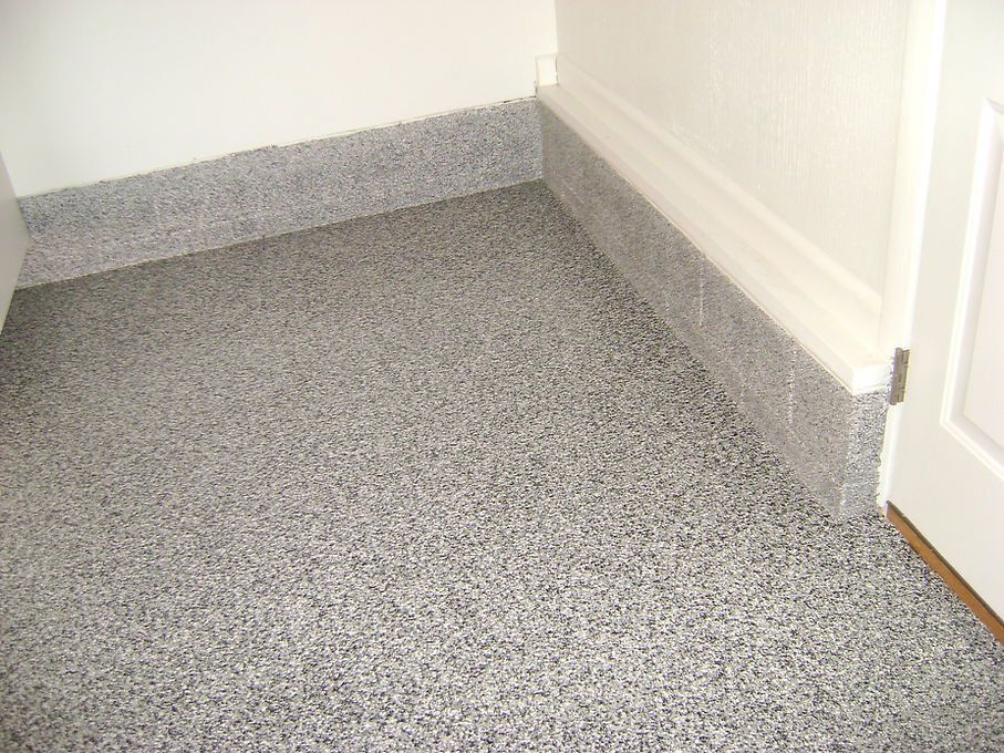 Gray speckled epoxy flooring and matching baseboards meet white walls and a doorway.