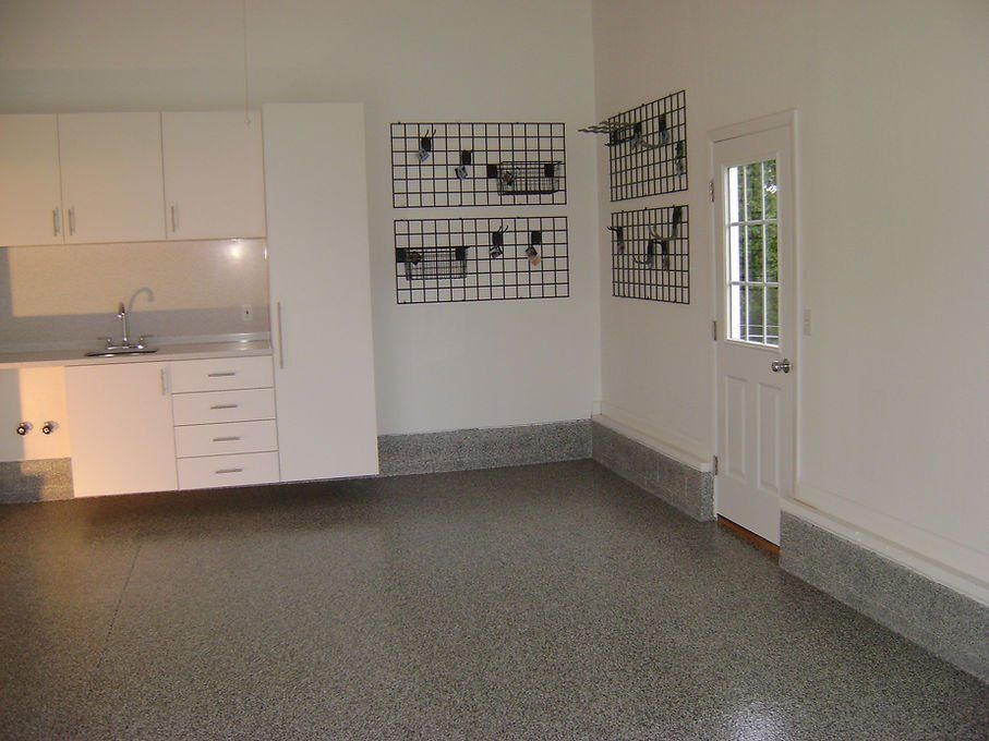 A clean, white garage with cabinets, a sink, and epoxy flooring. Features include artwork and an exterior door.