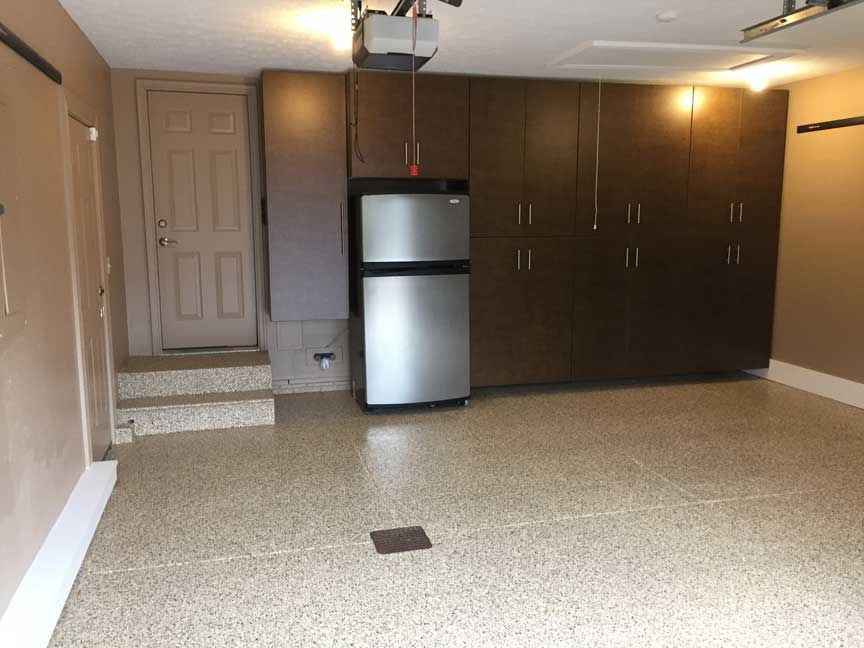 Garage interior with brown cabinets, refrigerator, and a speckled floor. Door and stairs on the left.
