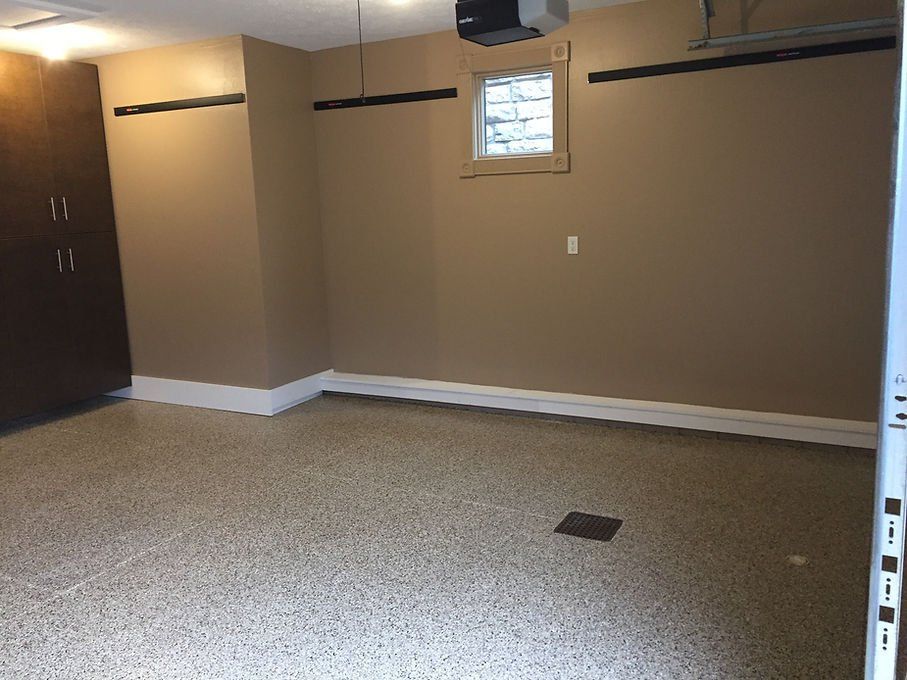Empty garage with speckled floor, tan walls, window, and storage cabinets.