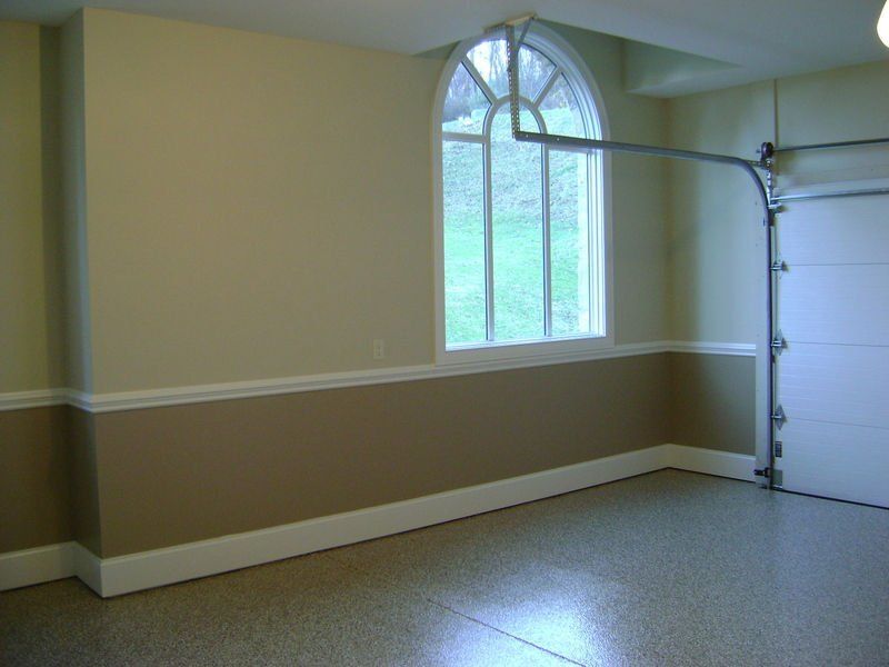 Empty garage with tan and cream walls, arched window, and epoxy floor. Garage door is visible.
