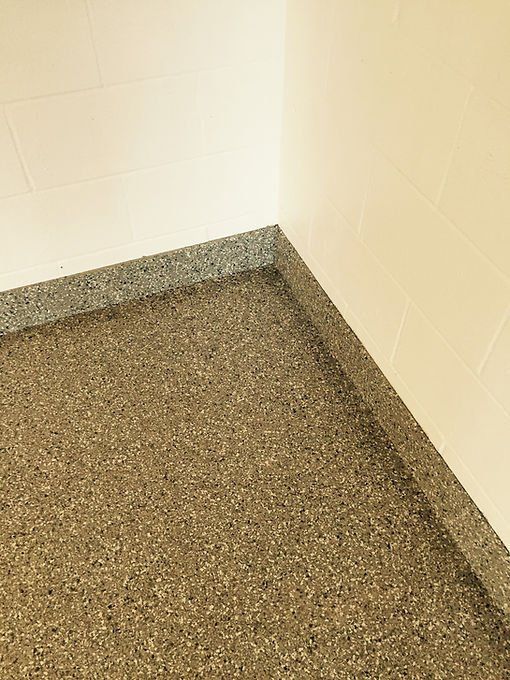 Corner of a room with speckled, gray-brown flooring and light beige walls.