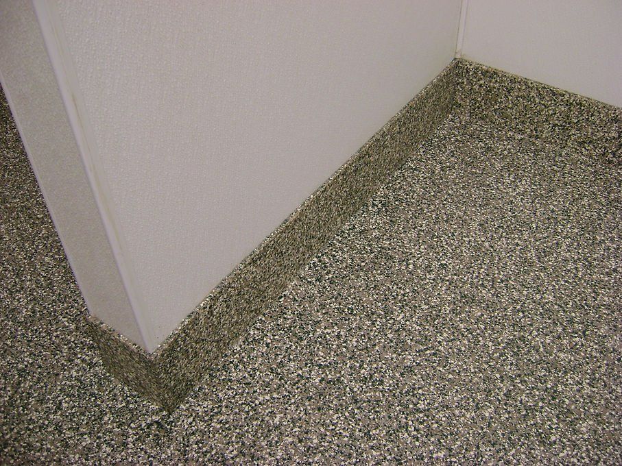 Corner of room with speckled floor and white walls.