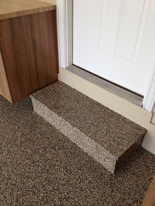 A step with a speckled surface leads to a white door. The floor and step have a matching speckled pattern.