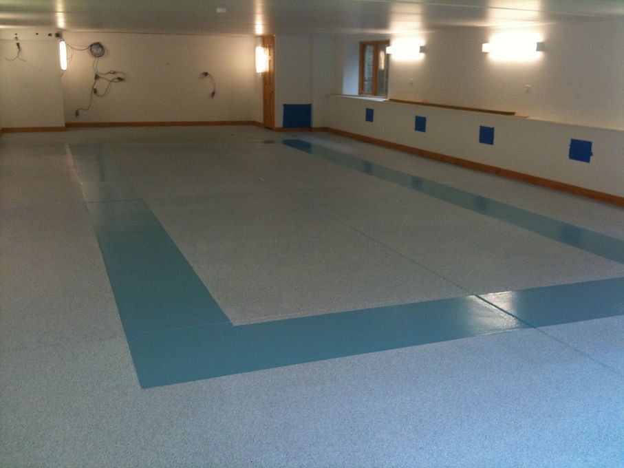 Empty indoor pool with blue painted border. White walls, overhead lighting.