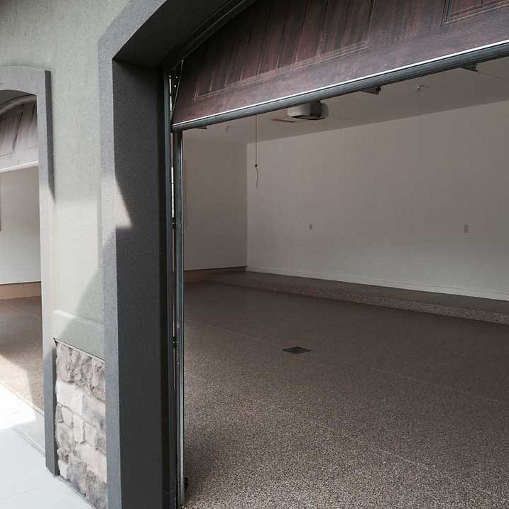 Garage interior with open door, light walls, and speckled floor.