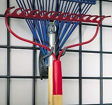 Red and blue garden rake hanging on a black grid wall.