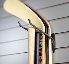 Black wall-mounted storage hook holding a wooden bat, hockey stick, and skis.