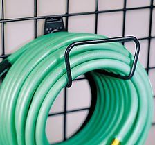 Green garden hose coiled on a black metal hook attached to a wire grid.