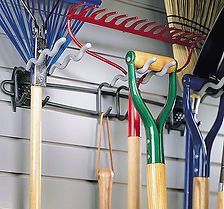 Garden tools hanging on a wall-mounted rack. Various tools in different colors, including rakes, brooms, and shovels.