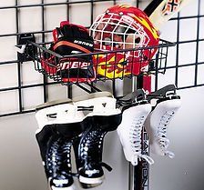 Hockey gear organized in a black wire basket and skate holders on a wall grid.