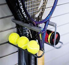 Tennis rackets, balls, and canisters stored on a wire rack attached to a wall.