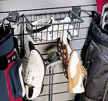 Golf gear storage: shoes hanging, balls and accessories in a wire basket on a wall-mounted system next to golf bags.
