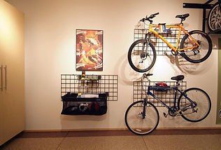 Two bikes hanging on a wall with storage. One is yellow, the other is blue. Accessories stored below.