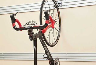 Black Pinarello bicycle hanging from a wall hook, front wheel in the air. Red and black handlebars.