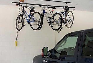 Overhead bike rack in a garage, holding three bicycles above a parked car.