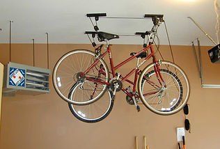 Two bicycles suspended from a ceiling-mounted hoist in a garage.