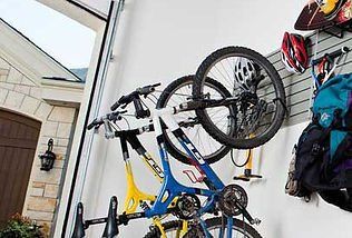 Bicycles hanging on wall-mounted racks in garage; helmets and gear also stored on the wall.