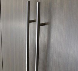 Two vertical, silver metal cabinet pulls on a textured, gray cabinet door.