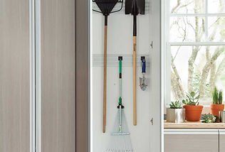 A white closet with gardening tools hanging. A window with plants is in the background.