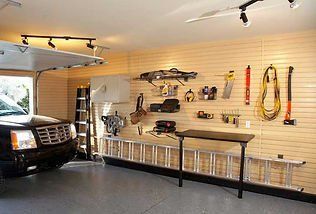 Organized garage with tools and ladder on slat wall. Black car parked inside, garage door open.