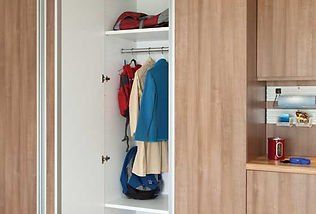 Closet with hanging coats, bags, and shelf, next to a counter with mounted organizers.
