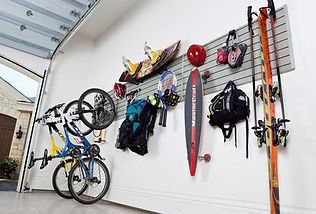 Garage wall storage system holding sports equipment: bikes, skis, skateboard, snowboard, helmets, bags.