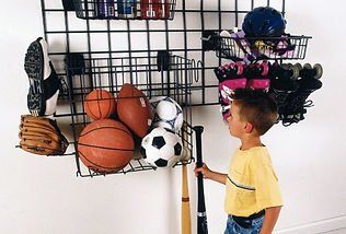 Boy looks at sports equipment organized on a grid wall in a room.